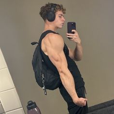 a man with headphones on taking a selfie in the mirror while wearing a backpack