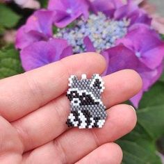 a hand holding a small beaded raccoon brooch with flowers in the background