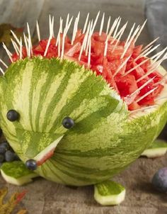 a watermelon sculpture with spikes on it's head and fruit in the shape of a hedgehog