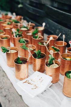 small copper cups filled with mint and lemonade on a white table cloth next to silver utensils