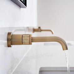 a faucet running water from a sink in a white tiled bathroom with gold fixtures