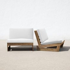 two wooden lounge chairs sitting next to each other on cement ground with white wall in background