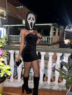 a woman wearing a mask and fishnet stockings standing on a balcony with her hands in her pockets