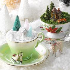 a cup filled with snow next to two small christmas trees on top of saucers