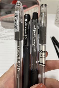 a person holding three different pens in their left hand and another pen on the right