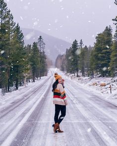 two people standing in the middle of a snow covered road with pine trees on both sides