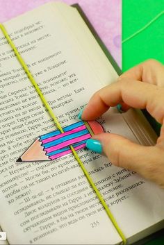 a person holding a pencil in their left hand and writing on an open book with colored paper