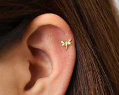 a woman's ear is adorned with a tiny gold leaf stud, which sits on top of her left ear