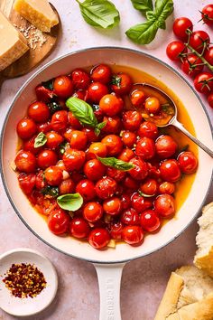 a pan filled with tomatoes and basil next to bread