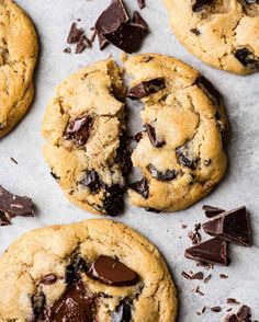 chocolate chip cookies with one broken in half and the rest on the counter top, surrounded by pieces of chocolate