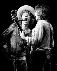 two men standing next to each other while one sings into a microphone and the other plays an electric guitar