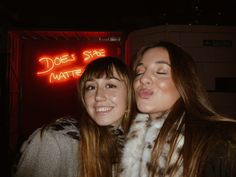 two women standing next to each other in front of a neon sign that says does she matter?