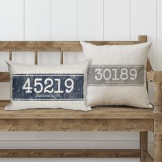 two pillows sitting on top of a wooden bench next to a white and blue pillow