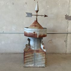 an old rusted water tower with arrows on it's top sits in front of a concrete wall