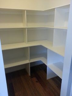 an empty closet with white shelves and wood flooring