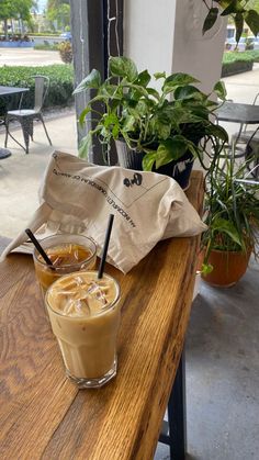 a cup of coffee sitting on top of a wooden table next to a bag and potted plants