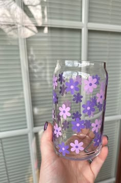 a hand holding a glass with purple flowers painted on the outside and inside, in front of a window