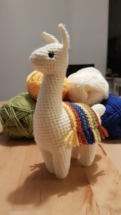 a crocheted llama sitting on top of a wooden table next to balls of yarn