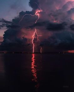 a lightning bolt is seen in the sky over water at night with dark clouds and bright lights