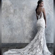 a woman in a white wedding dress standing against a wall with her back to the camera