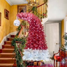 a decorated christmas tree sitting on top of a red rug next to a stair case