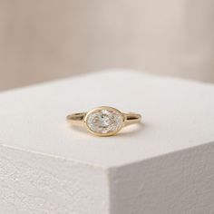 a yellow gold ring with a white diamond on top of a white box that is sitting on a table