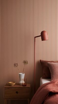 a bed with pink sheets and pillows next to a lamp on a nightstand in front of a striped wall