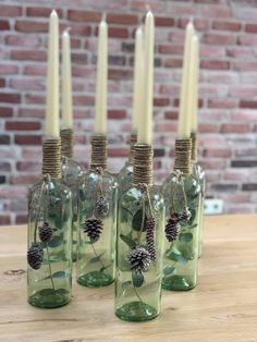 four green glass bottles with pine cones and leaves in them, sitting on a wooden table