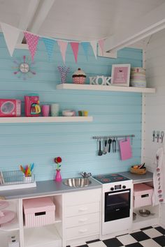 a play kitchen with blue walls and white cabinets, black and white checkered floor