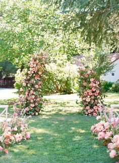 an outdoor ceremony setup with white chairs and pink flowers on the grass, surrounded by trees