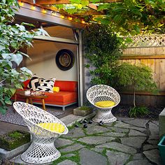 an outdoor living area with two chairs and a couch in the back yard, surrounded by greenery