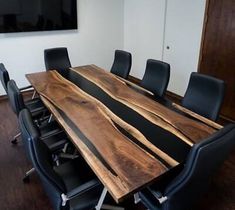 a wooden table with black leather chairs in an office setting, next to a flat screen tv mounted on the wall