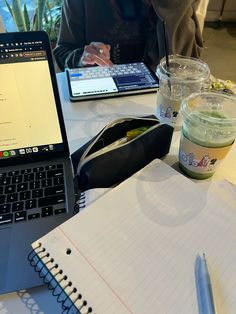 a laptop computer sitting on top of a table next to a cup of coffee and a notebook