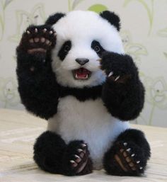 a stuffed panda bear sitting on top of a bed with its paws in the air