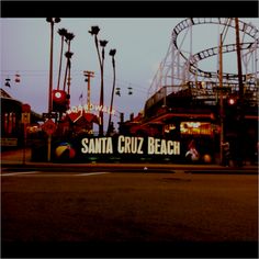 the santa cruz beach sign is in front of an amusement park roller coaster at dusk