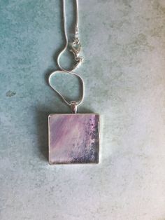 This is a portion of an acrylic pour that has been set in a silver plated bezel and coated with resin. The pour is different thicknesses so part of the silver bezel shows through for texture and added interest. This is such a pretty necklace in soft shades of lilac and little glimpses of a darker blue and is just what you need to compliment your spring wardrobe. This pendant is perfect for any female in your life, any occasion, but would be perfect for Mother's Day. Every care has been taken to capture the colours of this one off piece of jewellery, but bear in mind all screens and monitors are different. It is not recommended that you wear this jewellery in water. Artsy Purple Jewelry For Gifts, Modern Resin Jewelry For Gifts, Modern Resin Jewelry Gift, Silver Square Pendant Keepsake Jewelry, Silver Square Pendant Jewelry Keepsake, Silver Square Pendant Jewelry For Keepsake, Rectangular Silver Jewelry Gift For Her, Artsy Silver Jewelry With Large Pendant, Rectangular Resin Jewelry Gift