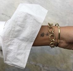 a woman's arm with two gold bracelets and a cross tattoo on it