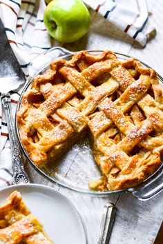 an apple pie with one slice cut out and two plates on the table next to it