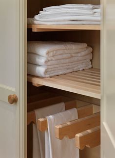 folded white towels are stacked on wooden shelves in a closet next to an open door