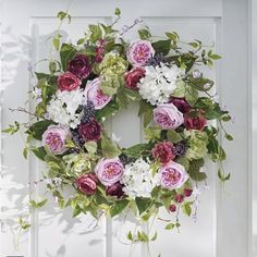 a white door with a wreath on it and flowers hanging from the front door handle