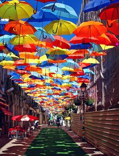 many colorful umbrellas are hanging from the ceiling in an alley lined with tables and chairs