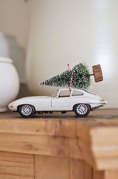 a white toy car with a christmas tree on the roof is parked in front of a vase