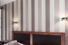 a bedroom with striped wallpaper and wooden headboard, along with two lamps on either side of the bed