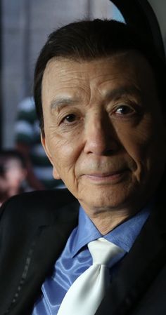 an older man in a suit and tie looking at the camera while sitting in a car