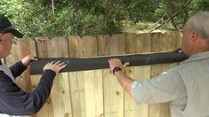 two men are working on a wooden fence