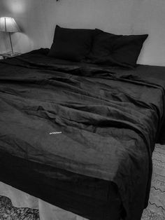 a bed with black sheets and pillows in a room next to a lamp on the floor