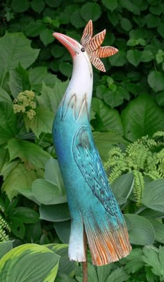 a blue bird statue sitting on top of a wooden stick in front of green leaves