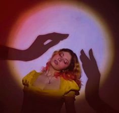 a woman standing in front of a light with her shadow on the wall