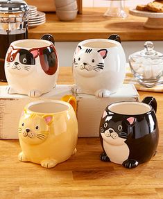 four ceramic cat mugs sitting on top of a wooden table