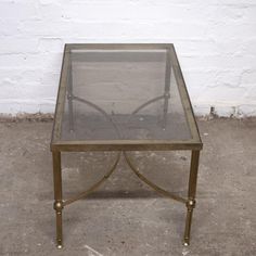 a glass and brass coffee table with metal legs on concrete floor next to white brick wall